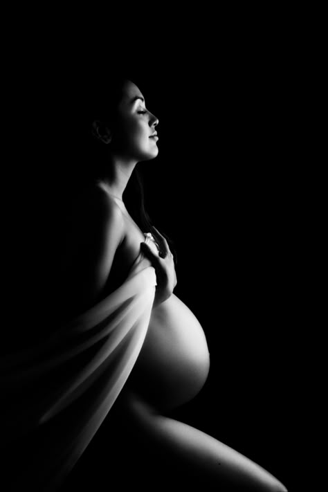 Pregnant woman holding white fabric over her breasts on a black background with light catching her legs & face. Black Women Maternity Shoot, Photoshoot In London, Maternity Silhouette, Studio Maternity Shoot, Maternity Photoshoot Ideas, Maternity Studio Photoshoot, Photoshoot London, Studio Maternity Photos, Maternity Photography Poses Outdoors