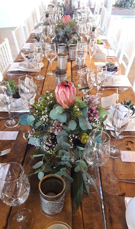 This style of table decor is so popular and looks so beautiful in the form of a table runner. It includes a range of different varieties of proteas, fynbos and greens in separate trays.  #Fynbos #Spring #Flowers #FabulousFynbos Protea Themed Wedding, Botanical Wedding Table Decor, Protea Wedding Table Decor South Africa, Protea Table Decor, Protea Wedding Table Decor, Protea Flower Arrangements, Fynbos Wedding, Fall Wedding Place Settings, Protea Wedding