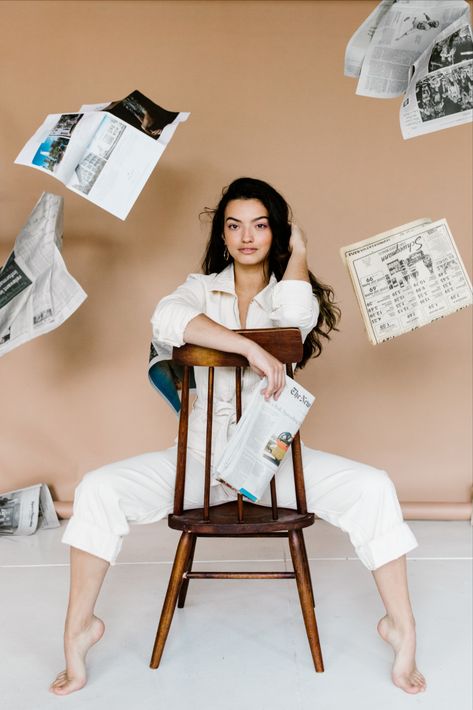 Female model in a cream Free People Utility Jumpsuit sitting on a backward chair with newspapers flying in the air. Newspaper Editorial, Newspaper Photo, Studio Photoshoot Ideas, Brand Photography Inspiration, Beautiful Photoshoot Ideas, Studio Photography Poses, Utility Jumpsuit, Business Photoshoot, Branding Photoshoot Inspiration