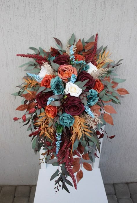 This cascading fall wedding bouquet is a captivating masterpiece, featuring a rich and moody color scheme that marries dark teal, rust, and burgundy flowers. The bouquet's lush design exudes a sense of opulence and warmth, making it an ideal choice for a fall wedding. The deep, luxurious hues of dark teal, rust, and burgundy come together to create a truly dramatic and stunning arrangement, adding a touch of elegance to the autumn celebration. ○ Color: teal, rust, orange, burgundy, ivory, green ○ Personalization: I can make changes to your wishes ○ Processing time: 1 - 2 weeks ○ Shipping time: 7 - 14 business days NOTE  ○ I ship with REGISTERED mail and you will get a tracking number.  ○ All items will be carefully packed in special package materials.  ○ The actual color may differ slightl Wedding Color Earth Tones, Burgundy October Wedding, Dark Teal And Rust Orange Bouquet, Fall Wedding With Turquoise, Teal Spring Wedding Colors, Dark Teal And Burnt Orange Wedding Flowers, Navy Burgundy Orange Wedding, Burnt Orange And Teal Wedding Bouquets, Teal And Orange Flowers