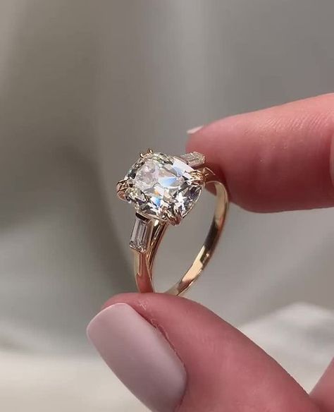 Frank Darling Custom Rings on Instagram: "Vintage diamond, modern twist.⁠ ⁠ Old mine cut diamonds have irregular facets that might not sparkle the way a modern brilliant diamond will, but these bulkier facets were meant to showcase the bright white colorlessness of the diamond and the way the stone will sparkle under the sweet and subtle luminance of candlelight.⁠ ⁠ There’s a reason these baddies are still around today. This three-stone engagement ring features a 3.27ct antique cushion a modified Harper setting, kept vintage with two tapered baguette side stones 😍⁠ ⁠ The Ring:⁠ • 3.27ct Antique-Inspired Elongated Cushion Cut Lab Diamond⁠ • G Color, VS1⁠ • 9.90 x 8.29 x 5.28 mm⁠ • 2mm Band⁠ ⁠ Mark your calendars, darlings! The last day for Valentine's Day proposal orders is January 23rd 💍 Cushion Elongated Engagement Ring, Baguette Setting Engagement Ring, Cushion Cut Engagement Ring Three Stone, Baguette Diamond Engagement Ring, Vintage Inspired Gold Engagement Rings, Cushion Cut Engagement Ring With Side Stones, Mine Cut Diamond Ring, Cushion Cut 3 Stone Engagement Ring, Antique Cut Engagement Ring