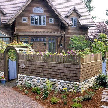 Combination Fieldstone and Wood Fence. If you love the look of stone and wood fencing, why not enjoy both? This fence features a low fieldstone wall topped with a wooden shake center and crowned with small pickets. A stone foundation makes the fence look solid and substantial. Round fieldstones are usually mortared into place because of their shape. Wood Fence With Stone Columns, Rock And Wood Fence, Stone Wall Outdoor Fence, Fieldstone Wall, Decorative Fencing, Picket Fencing, Stone Foundation, Stone Walls Garden, Building A Retaining Wall