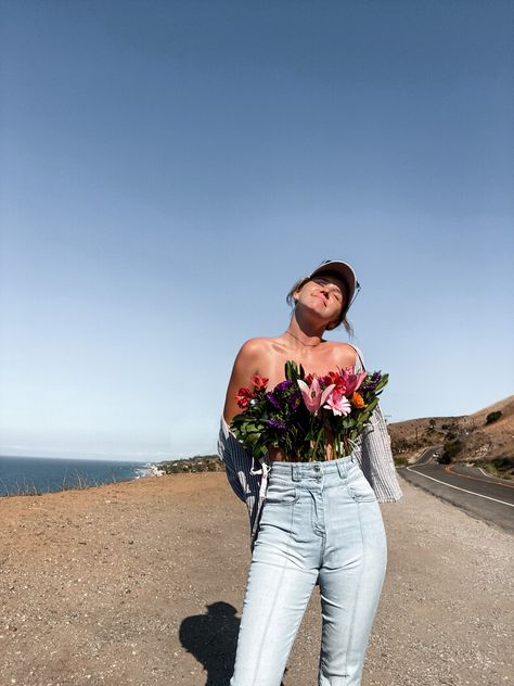 Young adult women wearing bell bottom jeans with bouquet of colorful flowers covering chest area with stems tucked into jeans creating a shirt affect, with button up drained off shoulders and ball cap on with Malibu canyon and ocean in the background Abstract Shirt, Flower Boquet, Beautiful Photoshoot Ideas, Photo Recreation, Create Shirts, Trader Joe’s, Instagram Aesthetic, Off Shoulder Blouse, Senior Pictures