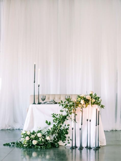 The sweetest sweetheart setup. Black and white candles and the table draped with fresh greens and creams flowers is the perfect neutral tablescape for your modern wedding. White Sweetheart Table Wedding, Rustic Sweetheart Table Wedding, Wedding Backdrop Sweetheart Table, Sweetheart Table Wedding Ideas, Candles Sweetheart Table, Black And White Sweetheart Table, Sweetheart Table Wedding Simple, Wedding Flowers Sweetheart Table, Sweetheart Table Wedding Elegant