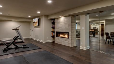 Just across the wall from the living area is the home gym. Separated from the rest of the space by a glass wall, the gym contains a television, built-in shelving for storage, work out machines and a sparring pad. The two-way fireplace pushes heat into this space, allowing the homeowner to get the most out of his workout. The glass wall that separates the spaces allows the gym to be visually connected to the rest of the basement, while remaining physically separated. Basement Workout Room, Basement Fireplace, Workout Room Home, Bamboo Room Divider, Basement Gym, Wooden Room Dividers, Basement Inspiration, Diy Basement, Basement House