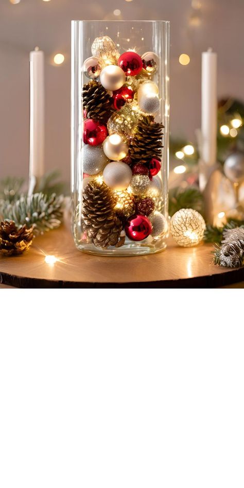 A tall, elegant glass vase filled with small, shiny Christmas ornaments, natural pinecones, and softly glowing fairy lights. The combination creates a warm and festive centerpiece for a holiday table Ornaments Table Decor, Christmas Centerpieces With Glass Vases, Christmas Centerpieces Ornaments, Pinecone Christmas Centerpiece, Christmas Decor Center Table, Christmas Cocktail Table Centerpiece, Floating Candle Centerpieces Christmas, Christmas Cheap Decorations, Simple Christmas Centerpieces For Party