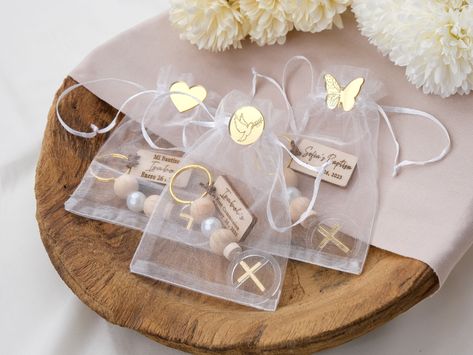 Looking for a meaningful way to say thanks to your baptism guests? Check out these awesome personalized baptism keychains. They are made of natural wood and pearl beads, and they have a rosary style with a cross at the end. You can also add a tag with the name and date of the baptism, to make them more personal. These keychains are not just pretty, but they also show your faith and appreciation. They are perfect for baptism favors, christening favors or recuerditos bautizo. You can also use them Cross Favors, Bautizo Ideas, Mini Keychain, Christening Favors, Baptism Favors, Party Favours, First Communion, Invitation Design, Pearl Beads