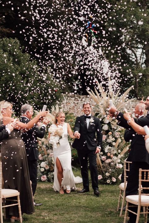 Groom in black tie walking back down the aisle in a front slit fitted wedding dress as white confetti explodes around them with pampas grass flower columns Flower Columns Wedding, Wedding Ceremony Confetti, Flower Columns, Groom Black Tie, Confetti Wedding Exit, Humanist Wedding Ceremony, Groom And Groomsmen Outfits, Bella Collina Wedding, Confetti Photos