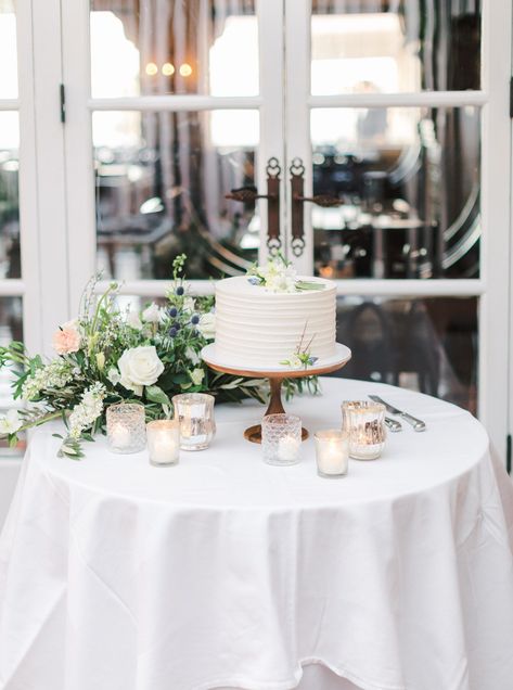 White one tier cake with ivory linen, green, peach, and ivory floral arrangements and mixed glass and metal votives. Intimate Wedding at La Valencia Hotel in La Jolla by Cavin Elizabeth Photography Wedding Cake Display Table, Wedding Cake Table Decorations, La Valencia Hotel, Intimate Winter Wedding, Wedding Cake Setting, Cake Display Table, Table Floral Arrangements, Wedding Cake Display, Single Tier Cake