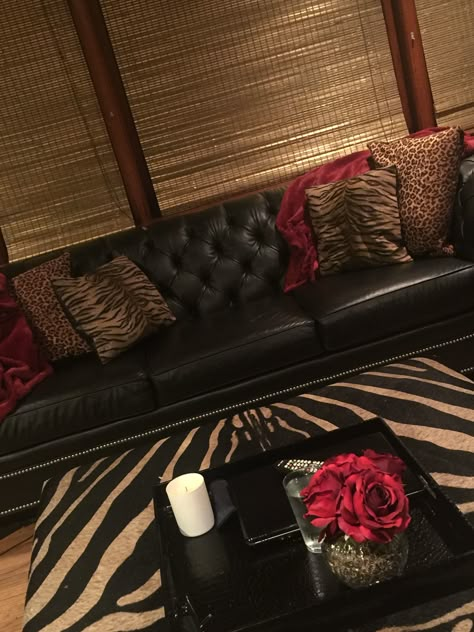 leather sofa with silver nail heads, leopard, tiger stripe pillows, red throw, zebra hide ottoman, red roses, black tray, white candle, Gold bamboo shades!!!All by Balance & Harmony Interiors!!!! 2000s House Aesthetic, Black And Red Living Room, Hide Ottoman, Candle Gold, Zebra Hide, Bar Aesthetic, Roses Black, Black Tray, Red Throw