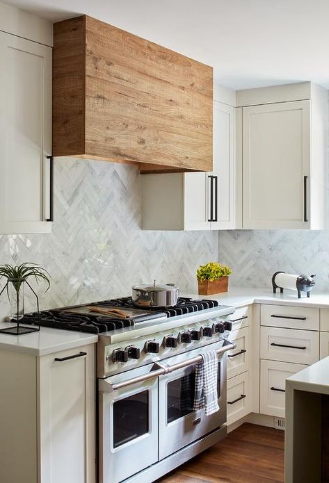 White and gray marble herringbone wall tiles hold a reclaimed wood range hood between white shaker upper cabinets finished with oil rubbed bronze pulls. Reclaimed Cabinets, Herringbone Wall Tile, Vintage Modern Kitchen, Backsplash White, Farm Style Kitchen, Kitchen Hood Design, Marble Herringbone, Tiles Backsplash, Herringbone Wall