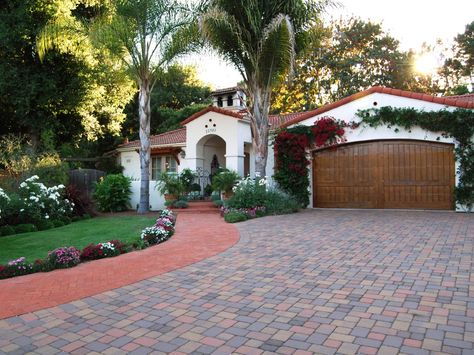 This Spanish Colonial Revival house with a barrel tile roof features a paver driveway, sidewalk and a wooden, arched garage door surrounded by bougainvillea. A mission parapet on top of the roof adds to the home's eclectic look. Colonial Revival House, Spanish Style Decor, Spanish Colonial Homes, Mediterranean Exterior, Spanish Decor, Mediterranean Home Decor, Small Backyard Gardens, Spanish Style Home, Casas Coloniales