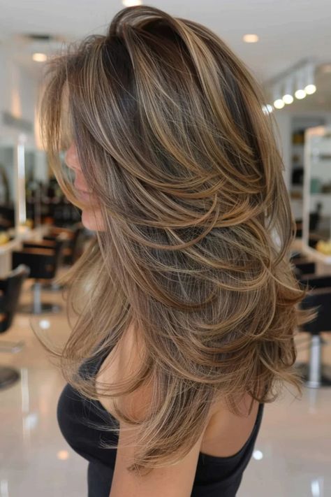 Woman with long, layered, brown hair with blonde highlights in a salon. Balayage In Layered Hair, Highlights And Low Lights On Brown Hair, Light Brown Hair With Highlights And Shadow Root, Brown Highlights With Layers, Cool Tone Brown Highlights, Ash Caramel Balayage, Highlights Brown Hair Bangs, Long Light Brown Hair With Highlights, Foil Highlights Brown Hair