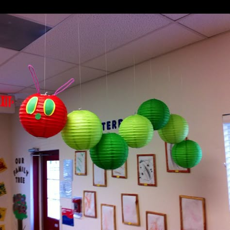 Very Hungry Caterpillar Mobile. Hang 8" lanterns (1 red, 6 in two shades of green) with different lengths of fishing line. Use pipe cleaners for antennae, and construction paper for eyes and nose. Makes me wish I taught primary again :) Preschool Classroom Themes Decorations, Treehouse Classroom, Classroom Aesthetic, Corridor Decor, Vbs 2025, Hungry Caterpillar Party, Infant Classroom, Hungry Caterpillar Birthday, Preschool Rooms