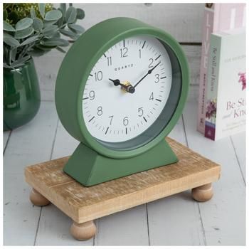 Dimensions: 6.75" H x 6" W x 2.25" D Power Source: 1 AA Battery (Not Included) Material: Metal & Plastic Shape: Round Color: Green, White, Black & Gold Orientation: Vertical Quantity: 1 Make sure you have enough time to get primped up and prepared with this Moss Green Metal Clock! This simple yet lovely clock features a round frame and an angled base in an eye-catching muted green. The white clock face has black numbers and hands that you can easily see. The backside is completed with a magnetic, hinged, metal flap that conceals the battery box. Place it on your desk, bathroom counter, or dresser so that you will be punctual.   Full Text:  Quartz White Clock, White Clocks, Black Numbers, Metal Clock, Muted Green, Bathroom Counters, Bathroom Counter, Table Clocks, Green Metal