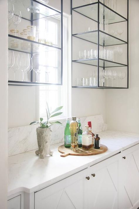 In this beautiful butler pantry, white walls frame two mounted iron and glass shelving units hung flanking a small window as a honed white marble countertop sits atop white cabinets finished with a diamond overlay and antiqued brass knobs. Glass Shelving Unit, Glass Shelves In Bathroom, Glass Shelves Kitchen, Glass Shelving, Wall Bookshelves, White Marble Countertops, Butler Pantry, Transitional House, Trendy Kitchen