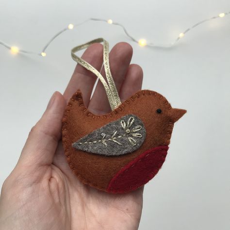 Made from 100% wool felt, this Robin tree decoration is completely hand stitched, embellished with simple embroidery in gold metallic thread. The catches the light beautifully, adding a lovely festive shimmer.   The robin measures 7cm / 3”. It is gently stuffed with toy stuffing, made from recycled plastic bottles!  The robin decoration hangs from a glittering gold ribbon so it can go straight onto the Christmas tree.   Your tree decoration  is posted to you 1st class, wrapped in tissue and popp Felt Xmas Ornaments Diy, Christmas Decorations Knitted, Handmade Fabric Christmas Decorations, Sew Christmas Tree Ornaments, Christmas Robin Decorations, Embroidered Tree Ornaments, Simple Felt Christmas Ornaments, Fabric Christmas Decorations Sewing, Easy Felt Christmas Decorations