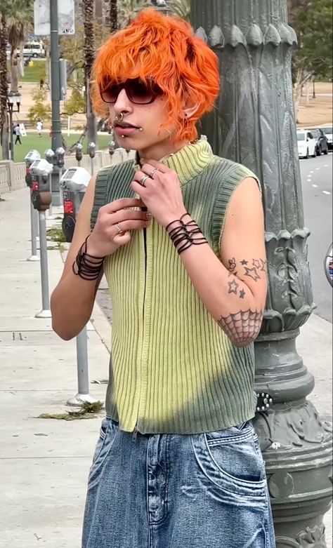 Jaded London Model with wavy, bright orange hair, piercings, dark sunglasses, tattoos, a tie dye zipper gilet/top, and baggy blue jeans. On the pavement in an English city Orange Hair Men, Orange Mullet Hair, Orange Hair Mullet, Black Red Orange Yellow Hair, Neon Orange Hair, Yellow To Orange Hair, Red Orange Yellow Hair Short, Bright Orange Hair, Baggy Blue Jeans