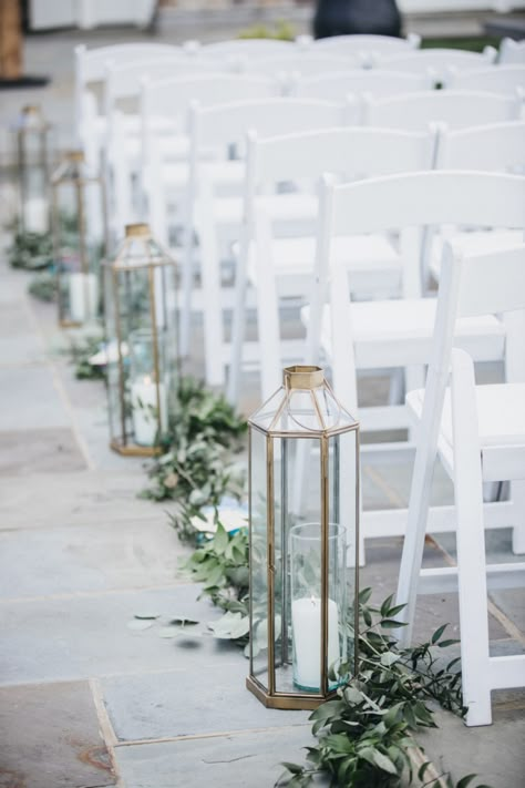 Aisle in ceremony lined with greenery and lanterns with candles Wedding Aisle Lanterns Outdoors, Lanterns Lining Wedding Aisle, Outdoor Wedding Aisle Decorations Summer, Lantern Lined Wedding Aisle, Beach Wedding Lanterns Aisle, Green Aisle Wedding, Greenery Lined Wedding Aisle, Lanterns For Wedding Aisle, Sage Green Outdoor Wedding Ceremony