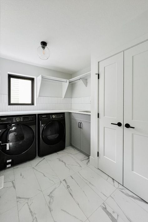 A clean and simple look is achieved with white marble floors, upper shelving with a place to hang dry clothing, and lower cabinets in a neutral grey tone. Custom Laundry Room, Lower Cabinets, White Marble Floor, Marble Floors, Simple Look, Low Cabinet, Laundry Room Design, Marble Floor, Grey Tones