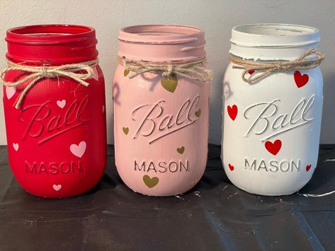 "Set of 3 hand painted \"Heart Theme\" mason jars.  Includes, white mason jar with red hearts, Ballet slipper pink jar with gold hearts, and red mason jar with light pink hearts  Each mason jar is hand painted with chalk paint, lightly distressed and sealed with clear wax for protection. They are decorated with decal hearts and hemp cord for the bow. Mason Jars are 16 ounces. If you have other colors in mind please feel free to send me a message." Red Mason Jars, Valentine Mason Jar, Saint Valentin Diy, Valentines Bricolage, Valentine Decoration, Valentines Party Decor, Valentine Centerpieces, Heart Theme, Valentines Baby Shower