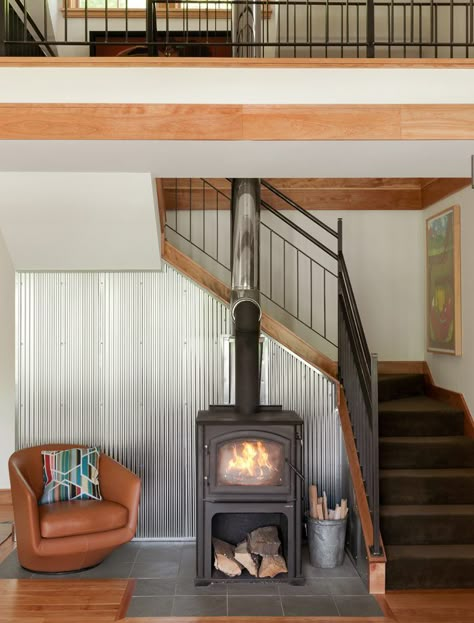 One of the favorite materials used is the narrow corrugated steel behind the wood stove - Fine Homebuilding #WoodStoves #Steel #Homes #Staircase #SingleFamilyHome #NewEngland #BeautifulHouses Fireplace By Staircase, Stairs Behind Fireplace Living Rooms, Wood Stove By Stairs, Wood Stove In Front Of Stairs, Fireplace Under Staircase, A Frame Wood Stove, Small Woodstove Living Room, Wood Stove Under Stairs, Staircase Behind Fireplace