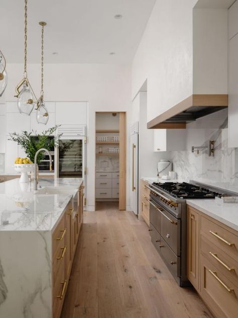 Light wood cabinets and a light hardwood floor contribute to the airy, open feeling in this white contemporary kitchen. The cabinets pair beautifully with white marble countertops, including the island, which houses a farmhouse sink. The marble backsplash behind the high-end range has a pot filler while the range hood has light wood trim for a seamless look with the rest of the space. Texas Lake House, Contemporary Farmhouse Kitchen, High End Kitchen Design, White Contemporary Kitchen, Kitchen Hood Ideas, Marble Floor Kitchen, Light Wood Kitchens, Marble Countertops Kitchen, Light Wood Cabinets