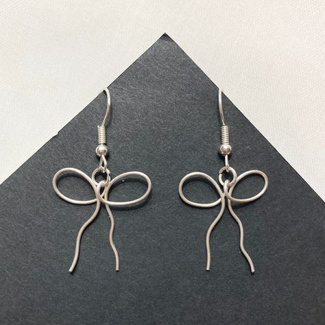 ✦ Dainty ribbon/bow earrings that will meet your coquette, dollcore, and balletcore needs!  ✦ New & handmade ✦ Handle with delicacy to avoid bending the wire! ✦ Imperfections & plier marks may be visible ✦ Silver/gold plated lead & nickel free zinc alloy hooks; 20 gauge wire ✦ Rubber backings included ✦ More jewelry on my shop; message for customs! Wire Keychain Ideas, Silver Wire Earrings Handmade, Wire Earing Tutorials, Handmade Wire Earrings Ideas, Diy Earring Hooks, Wire Shapes For Jewelry, Simple Wire Pendant, Metal Wire Earrings, Cute Wire Earrings