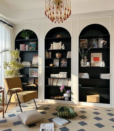 Picture of white arched bookcases with black backing and shelves, with amazing books and decor, a yellow chair and a rug for a reading nook Arch Top Bookcase, Corner Shelves Built In, Upstairs Reading Nook, Arched Bookcase Living Room, Arched Book Shelves, Two Tone Built Ins Bookshelves, Arched Library Wall, Arch Built In Shelves Fireplace, Arched Bookshelf Built Ins