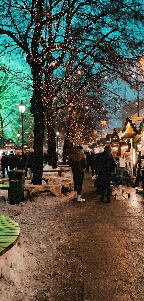 Trees are lit up with Christmas light and there are round benches around them. A wheel is lit green, on the left, not to far away. People are walking around in their warm clothing looking at the beautiful Christmas stands on the left and right side. Some snow laying here and there. Oslo Christmas Market, Oslo Christmas, Christmas In Norway, Norway Christmas, Christmas Feels, Oslo Norway, Funny Arabic Quotes, Scandinavian Christmas, Christmas Market