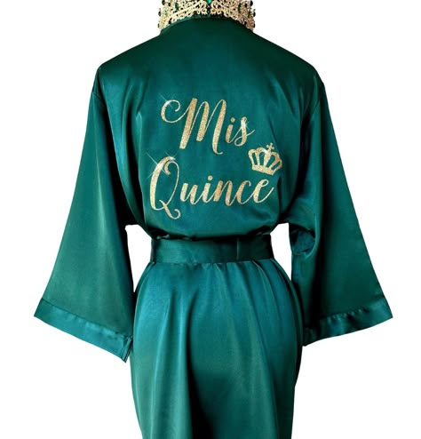 "Celebrate your special Quinceañera with our beautiful Mis Quince Satin Robe, a perfect addition to your memorable day! Crafted from high-quality soft silky satin, our Quinceañera robe ensures a luxurious and comfortable experience while getting ready for the celebration. Our robes come with inner side pockets!  Customize your robe with glitter text or mirror metallic for that extra touch of glamour! Choose from a variety of glitter or metallic options to make your Mis Quince Robe uniquely yours Emerald Dama Dresses, Emerald Green Surprise Dance Outfits, Emerland Green And Gold Quince Dress, Emerald Green Quince Robe, Quinceanera Silk Robe, Emerald Green Silk Robe Quince, Emerald Green And Gold Quince Crown, Quincenera Dresses Emeral Green, Quince Clothes