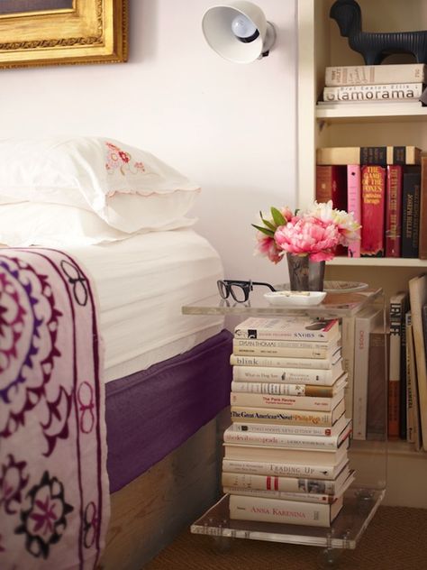 Sara Ruffin Costello - bedrooms - lucite nightstand, lucite bedside table, acrylic nightstand, acrylic bedside table, platform bed, gilt frame, purple sheets, purple quilt, pink and purple quilt, built in bookshelf, scalloped shams, scalloped bedding, Pretty Nightstand, Lucite Bed, Bedroom With Books, Bedside Books, Book Stacking, Bookshelf Nightstand, Bedside Table Styling, Reading Library, Book Table