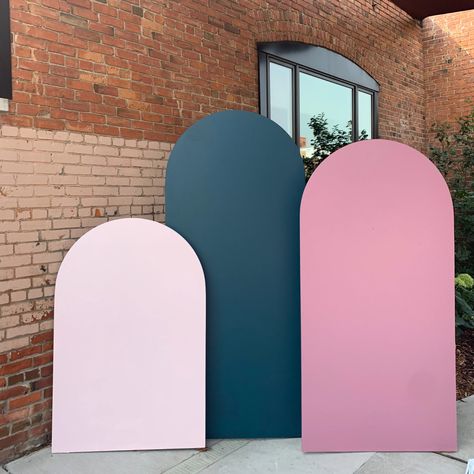 Photo shows three wooden arches of various sizes and colors propped against a brick wall. The far left arch is the shortest and is blush pink. The middle arch is a dark teal green and is the tallest arch. The far right arch is a middle tone pink mauve. Diy Tinsel Jacket, Diy Photo Backdrop Ideas, Photoshoot Backdrop Ideas, Chiara Arched Backdrop, Diy Arches, Diy Chiara Backdrop, Wedding Ceremony Backdrop Diy, Diy Tinsel, Photo Backdrop Ideas