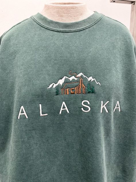 Our Tomorrow brand featuring an embroidered cabin in the mountains. Our Alaska sweatshirt is the perfect cozy sweatshirt. Comfort Colors sweatshirt 80% cotton, 20% polyester Premium heavy fabric Vintage Alaska Sweatshirt, Cabin Sweatshirt, Alaska Sweatshirt, Alaska Outfits, Crewneck Aesthetic, Cabin In The Mountains, Mountain Shirt, Comfort Colors Sweatshirt, Fashion Aesthetics