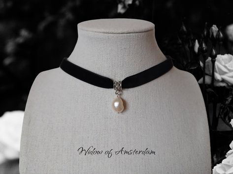 You can choose your own pearl, how cool is that?!

This black velvet choker features a single, real freshwater pearl pendant hanging from the center. The pendant is attached to the choker with a decorative bail, which has an intricate design that adds to the overall elegance of the piece. The pearl itself has a creamy white color, which contrasts beautifully with the dark choker. The overall aesthetic is sophisticated and classic, with a touch of gothic elegance due to the black choker. Gothic Elegance, Ribbon Choker, Black Velvet Choker, Velvet Choker, Black Choker, 90s Nostalgia, Royal Jewelry, The Pearl, Dainty Jewelry