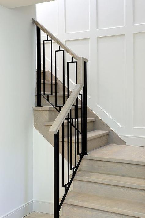 A gray wash wood staircase is finished with hollow iron balusters alongside a staircase wall clad in wainscoting. Modern Stair Railing, Diy Wainscoting, Iron Staircase, Iron Stair Railing, Stair Railing Design, Staircase Remodel, Staircase Wall, Wood Staircase, Stair Remodel