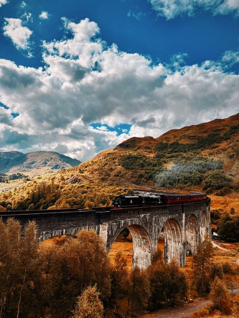 Steam train travelling over bridge, orange and red trees and hills surround. Hogwarts Fall Wallpaper, Autumn Hogwarts, Harry Potter Autumn, Hogwarts Autumn Wallpaper, Autumn At Hogwarts, Hogwarts Landscape Wallpaper, Harry Potter Scenery Backgrounds, Fall At Hogwarts Aesthetic, Fall Cover Photos