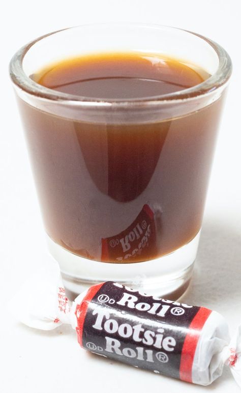 A shot glass filled with a brown tootsie roll shot on a white background next to a piece of tootsie roll candy. Tootsie Roll Shot Recipe, Tootsie Roll Drink, Circus Drinks, Tootsie Roll Shot, Drinks For A Party, Delicious Shots, Spring Drinks, Mixology Recipes, Spring Drink