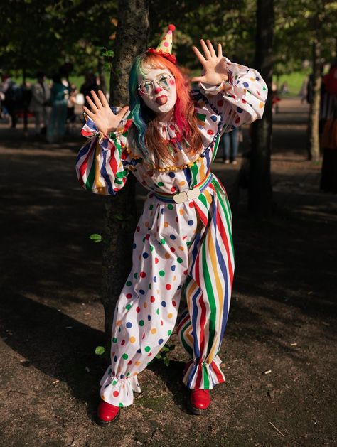 Girl in a white clown suit, half spotty, half stripey with primary colours. She has rainbow hair and a little hat and red shoes Clowncore Halloween Costumes, How To Make Clown Costume, Clown Outfit Reference, Clown Halloween Costumes Cute, Clown Outfit Inspiration, Rainbow Clown Outfit, Cute Clown Outfit Aesthetic, Halloween Costumes Clown Outfit, Vintage Clown Halloween Costume