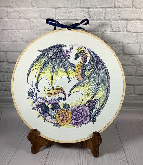 This floral dragon design is embroidered onto white colored cotton canvas and stretched into an 10 inch hoop.  There is a backing on the hoop.  Embroidery hoops are so easy to display.  You can use a plate display stand, or simply tap a hanging nail into the wall and slip the hoop over it. Pricing is determined by the stitch count.  Many of the designs are very detailed and can have over 60,000 stitches and some even more than that!  Please note that the designs are made to order, colors may vary slightly.  If you would like a different color ribbon,  specify in the personalization area. I have tons of designs, if you are interested in another subject or theme, contact me.  I would love to work with you to find the perfect home decoration or gift. Cute Dragon Embroidery, Dragon Embroidery Pattern, Watercolor Embroidery, Floral Dragon, Embroidery Decor, Embroidered Dragon, Dragon Embroidery, Cross Stitch Tutorial, Dragon Decor