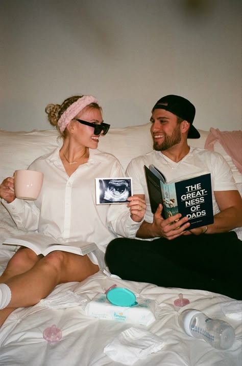 Husband and wife announce pregnancy sitting on bed. Husband reads book titled “The Greatness of Dads”, while wife holds ultrasound photo in her left hand, and pink coffee mug in her right. The bed has scattered diapers, pink pacifiers, baby wipes, bottles and clothes. Intimate Pregnancy Announcement, Pregnancy Announcement Nails, Pregnant Surprise Family, Family Pictures Pregnancy Announcement, Announce To Family Your Pregnant, Italy Pregnancy Announcement, Modern Pregnancy Announcement, Discreet Pregnancy Announcement, Revealing Pregnancy To Family