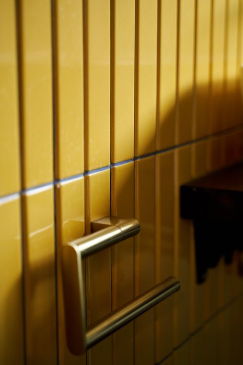 A close-up view of vibrant mustard yellow vertical tiles in a bathroom, paired with a sleek brushed brass towel rail. The tiles have a glossy finish, reflecting light and adding depth to the wall. The combination of bold color and luxurious brass accents creates a striking, contemporary look, perfect for adding warmth and style to a modern bathroom space. The shadows cast on the tiles enhance their textured appeal, making the brass pop against the rich yellow background. Mustard Yellow Bathroom, Small Family Bathroom, Chic Modern Bathroom, Family Bathroom Design, Yellow Bathroom Tiles, Unique Bathrooms, Brushed Brass Hardware, Chevron Tile, Traditional Bathrooms