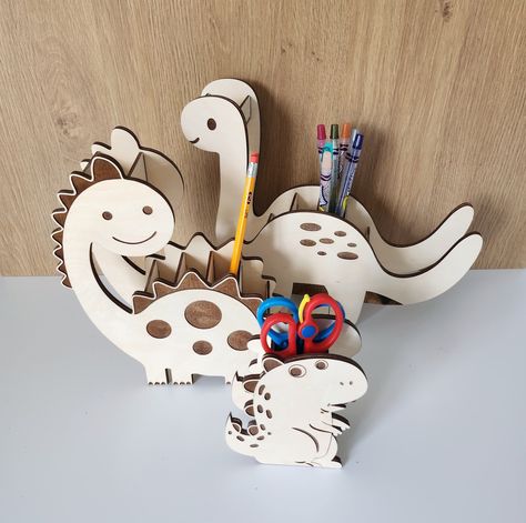 "Make your child's desk fun and to their liking with these cute dinosaur organizer sets. Choose between T-rex, Longneck, and Spikey Longneck (tarbonosaurusor, padasaurus/brachiasaurs, and dippladapolis if you ask my boys 😅) or get the set for a discount! Longneck measures 9\"x8.5\"x2.5\". T-rex measures 5\"x4.5\"x2\" Spikey Longneck measures 10.5\" wide x 9.5\" high x 2.5\" deep" Marti 8, Dinosaur Pencil, Diy Montessori Toys, Wooden Dinosaur, Wooden Desk Organizer, Door Signs Diy, Laser Cut Wood Crafts, Caddy Organizer, Laser Ideas