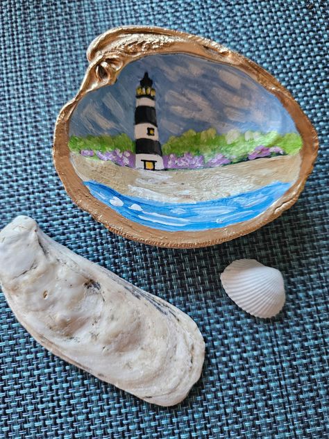 Hand-Painted Lighthouse on Seashell  Capture the serene beauty of the coast with this exquisite hand-painted seashell featuring a charming lighthouse.  Each shell is meticulously hand-painted, making it a unique and one-of-a-kind piece of coastal art.  This is an Original Work of Art--not decoupaged.   This sturdy shell makes a fun splurge for yourself or a memorable gift for a special person. Use as decor or as a ring or trinket dish. Your shell comes in a complimentary drawstring pouch. Lighthouses symbolize strength and guidance. Each shell is hand painted in my smoke-free studio in beautiful Fenwick Island. I find all my shells for painting along the Delaware coast. I used acrylic paint in the creation of this Lighthouse shell, then I sealed the shell with clear satin sealer. To see mo Painting On A Seashell, Cute Shell Painting Ideas, Painted Shell Ornaments, Clamshell Crafts, Projects With Shells, Painting Shells Ideas, Sea Shell Painting Ideas, Painted Sea Shells Ideas, Seashell Art Painting