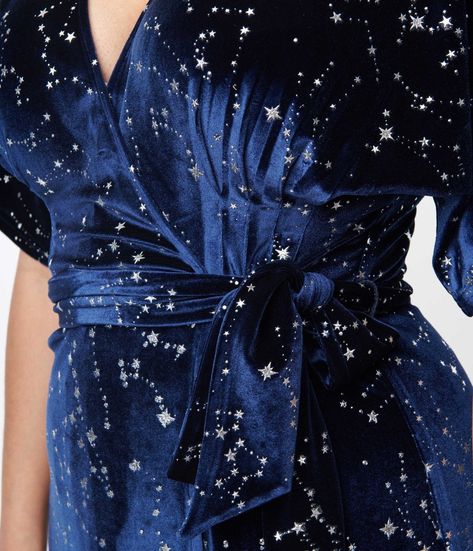 Wrap yourself in stars, dears! This sensational 1970s style wrap dress from Unique Vintage is crafted in a gorgeous navy blue velvet that dances with twinkling silver stars throughout. The sultry wrap design is secured with dual buttons creating a surplice neckline that is framed by dolman sleeves. The seamed high waist is cinched by a matching self tie sash while the skirt cascades to a sweeping midi silhouette!Available in sizes XS-5X while supplies last. Holiday Cocktail Dress Plus Size, Blue 1920s Dress, Celestial Outfit Aesthetic, 70s Dresses Formal, Feyre Dress, Dune Fashion, Celestial Outfit, Celestial Gown, Dark Blue Velvet Dress