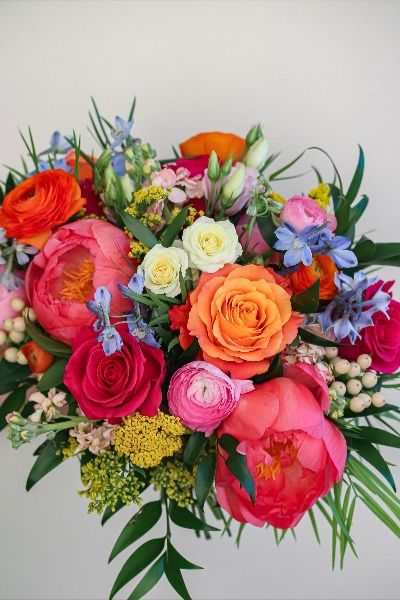 A sweet and colorful summer bouquet featuring 'coral charm' peonies, 'free spirit' roses, delphinium, yarrow, ranunculus, hypericum, 'avery' spray roses and beautiful lisianthus! Bright Peony Bouquet, Wedding Bouquets Wild Flowers Simple, Multicolor Prom Bouquet, Colorful Ranunculus Bouquet, Colorful Floral Bouquets, Bright Pink Roses Bouquet, Wedding Bouquets Peonies And Roses Ranunculus, Bright Flowers For Wedding, Bright Bouquet Of Flowers