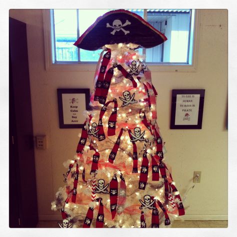 Pirate Christmas Tree! I decided to go with our Mascott this year. Cost...$0 My students faces...priceless! My mother-in-law gave me the pre-lit tree, already had the fabric, cut into strips and tied on the tree, toile ribbon in red and black....got that from my wife's stash, inflatable pirate hat, and bulletin board Jolly Roger's made into ornaments! Pirate Themed Christmas Tree, Pirate Ornaments Diy, Pirate Christmas Tree, Pirate Ornament, Christmas Pirate, Pirate Christmas, Pirate Theme Classroom, Pirate Ideas, Pirate Classroom