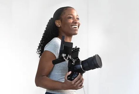 A vibrant and enthusiastic female videographer smiling while holding a professional video camera in a modern studio setting. The image captures the essence of creativity and professionalism in video production, highlighting the role of skilled videographers in producing high-quality content for marketing and media purposes. Freelance Videographer, Brand Image, Video Production, Video Content, Professions, Visual Art, Latest Trends, Drive, Marketing