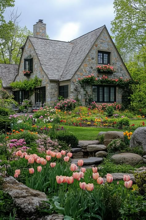 English country house with stone siding multi pitch roof green living wall lush garden with rocks and wildflowers tulips roses. Discover the charming essentials and cozy vibe that make a cottagecore house your perfect rural escape. Houses In The Woods Country, English Rock Garden, Beautiful English Gardens, Country Side Homes Cottages, Country Side House Aesthetic, Cotswolds England Cottage, Cottagecore Aesthetic House Outside, Houses Exterior Cottagecore, Big Cottagecore House