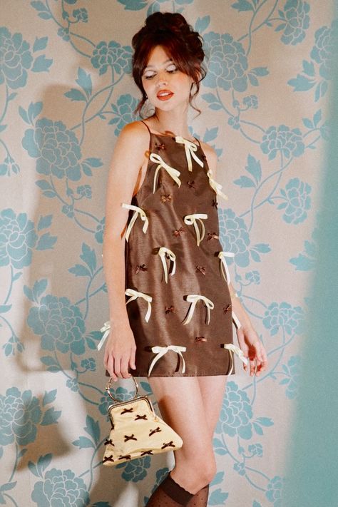 We absolutely adore our brown dupioni mini dress. From our latest collection inspired by retro catalogue fashion, it features a flattering A-line silhouette and is hand-embellished in brown and pastel yellow bows. It is fully lined and has a back concealed zip. Choose your usual size. Those with curvier hips may wish to choose the next size up. Please allow 21 business days from purchase for us to ship, as this dress is made to order. Made in England. We will email you after your purchase in ord Fashionable Halloween Costumes, Ribbon Dress Fashion, How To Order Design, Retro Catalogue, Clothes With Bows, Pastel Mini Dress, 60s Inspired Fashion, Retro Chic Fashion, Bow Embellishments